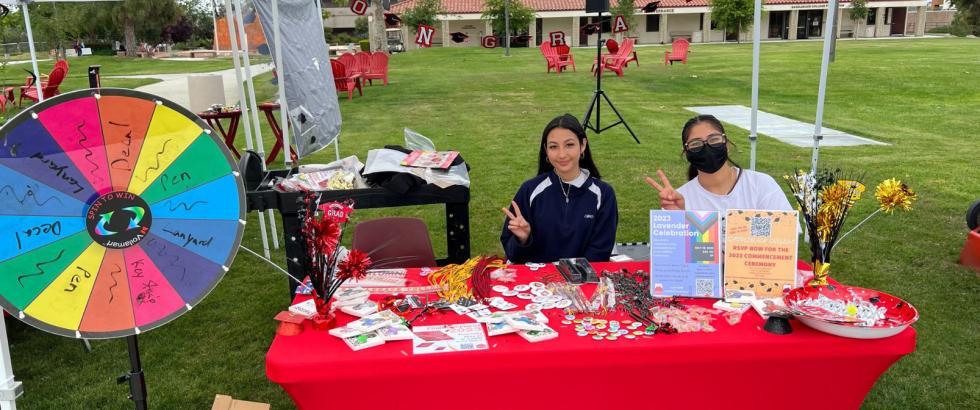 Two students sit at a table with a red table cloth decorated with various graduation decorations.