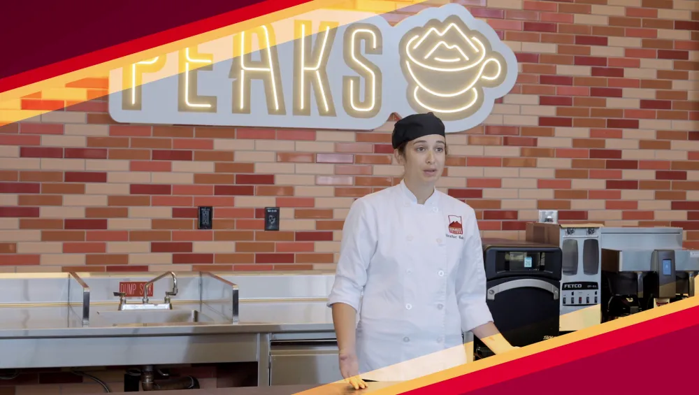 Female student being interviewed in behind counter in front of Peaks Cafe sign.