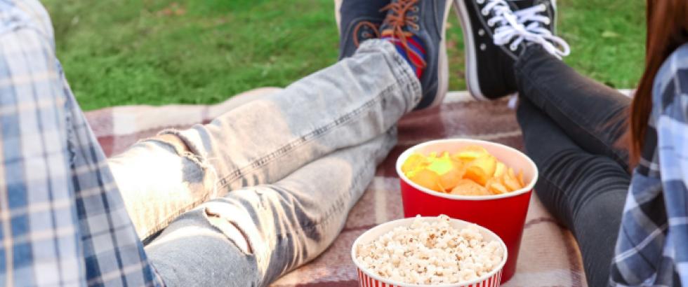 Two students sitting with their ankles crossed on a blanket with snacks between them