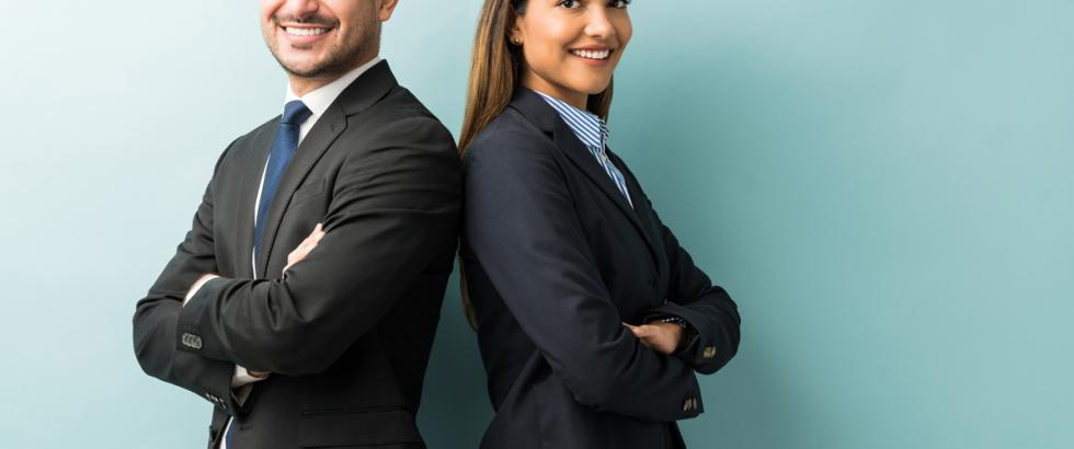 Man and woman dressed in business attire standing back to back and smiling