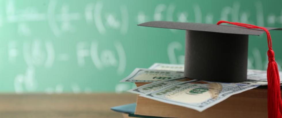 A stack of textbooks, with a few $100 dollar bills on top of it and a mortar board resting on top of the money.