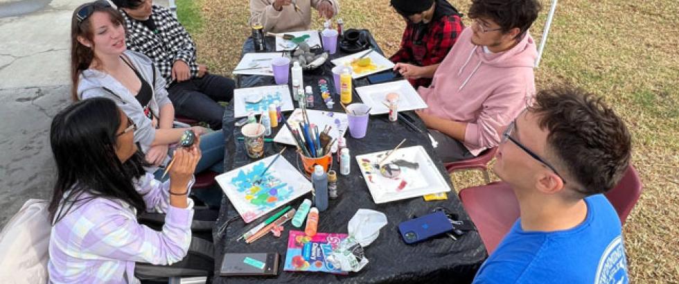 Students sitting at a table on the Quad participating in rock painting.