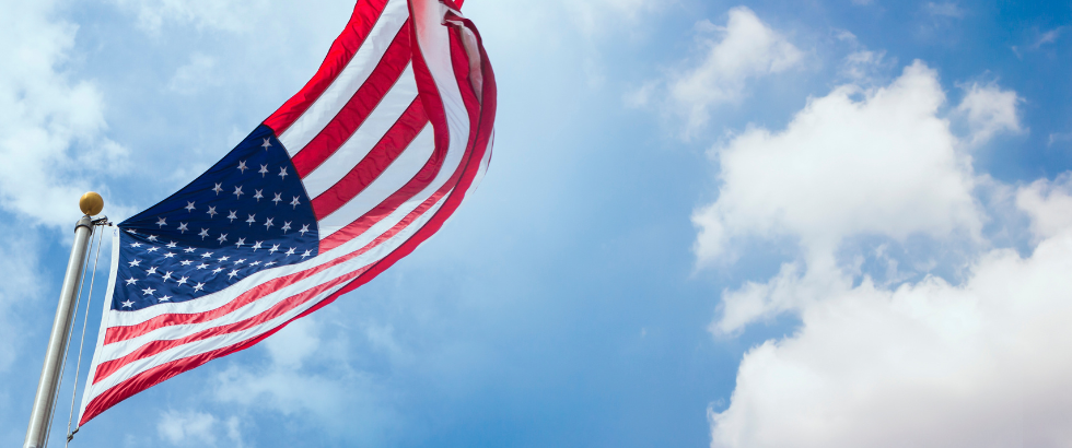 American flag waving with blue sky and cloud behind