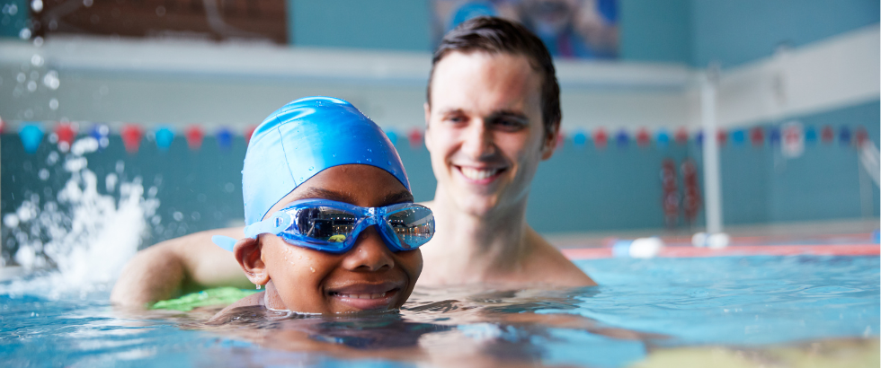 male swimming coach giving boy holding float one to one lesson in pool