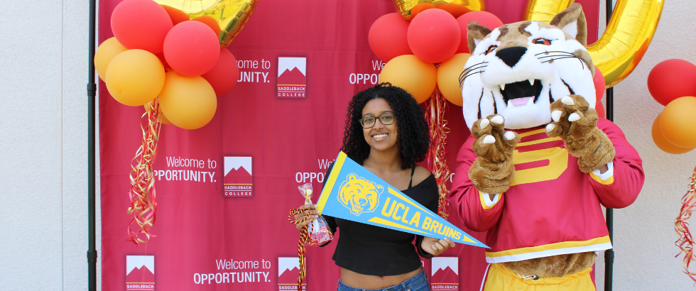 saddleback college mascot, blaze the bobcat, standing with a female student holding a UCLA pennant
