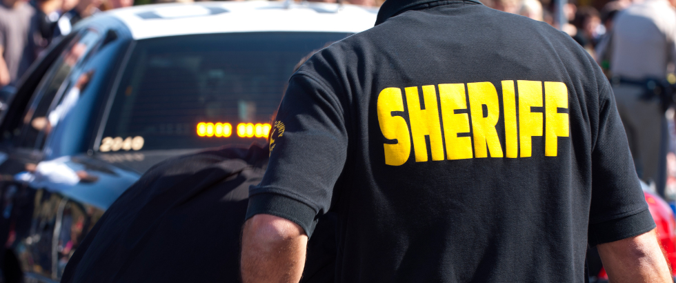 rear view of sheriff behind patrol car watching suspect.