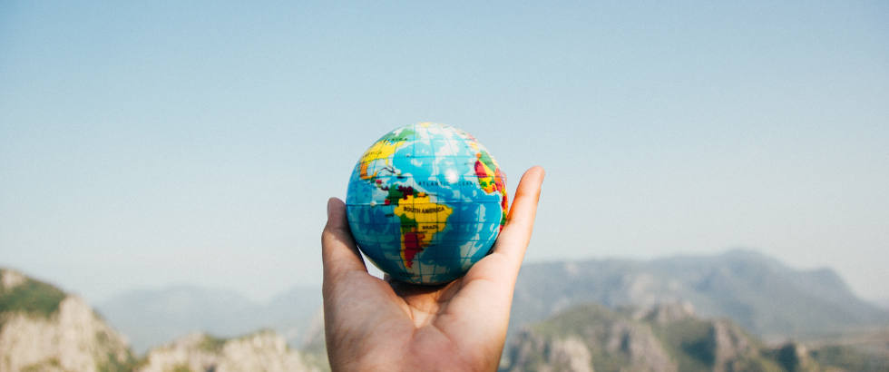 hands holding earth globe in front of mountains