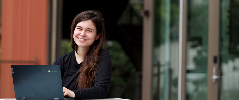 image of a female student sitting at a table outside of the gateway building with her laptop