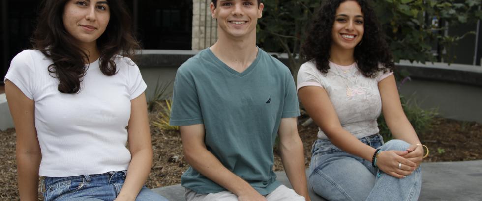 Three students sitting on the planter box smiling at camera