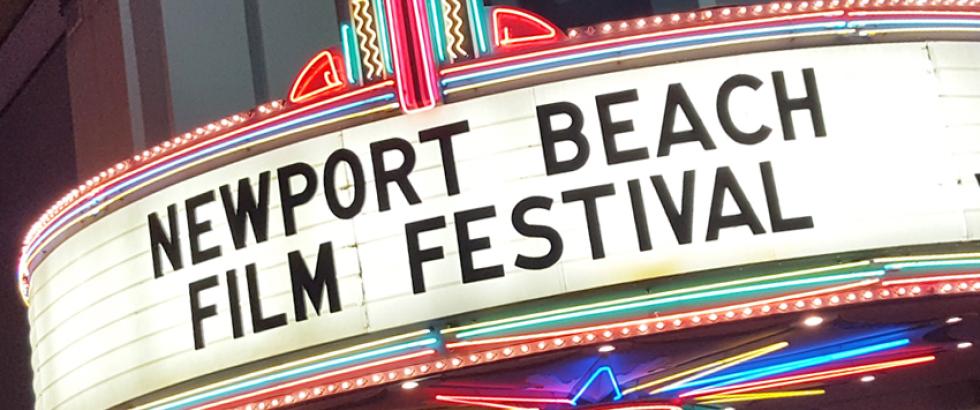 Movie theater marquee with the text: NEWPORT BEACH FILM FESTIVAL in all black caps. bright, lit sign is surrounded by colorful neon lights
