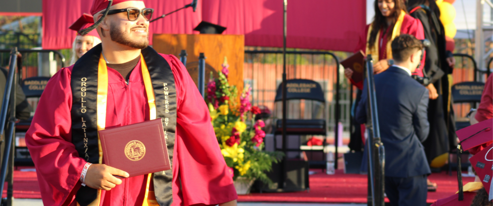Male student smiling and looking into the crowd after receiving his diploma cover at Saddleback College commencement.