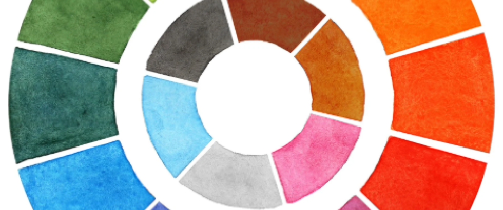 Circular color wheel made of painted swatches arranged in two rings. The outer ring transitions through green, yellow, orange, red, purple, and blue segments, while the inner ring shows smaller sections in gray, brown, blue, pink, and neutral tones on a white background.