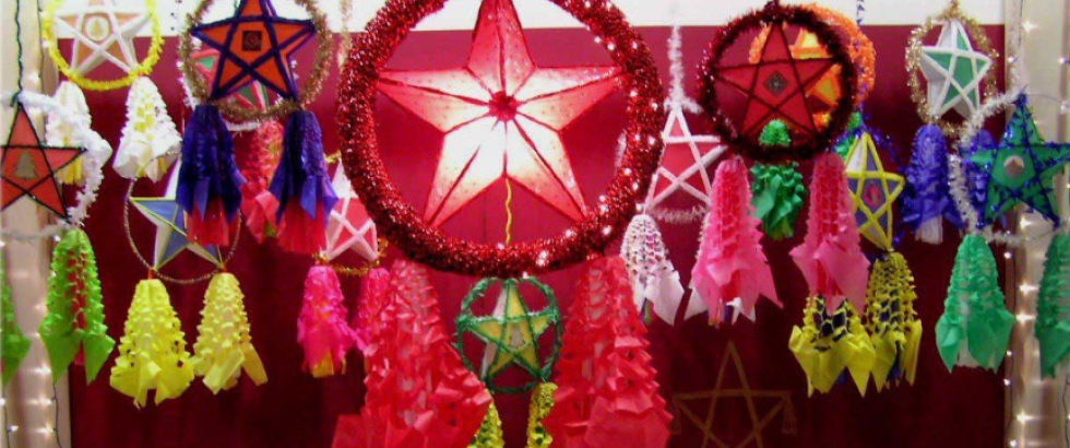 Colorful star-shaped lanterns and hanging decorations in red, pink, yellow, green, blue, and purple fill a festive display. A large illuminated red star framed by red tinsel hangs in the center.
