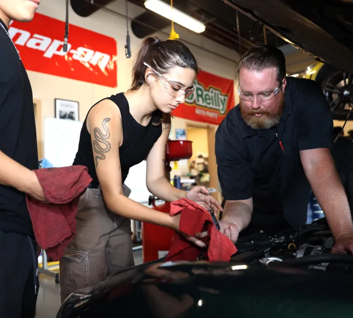 Two students with an instructor working on a car engine,