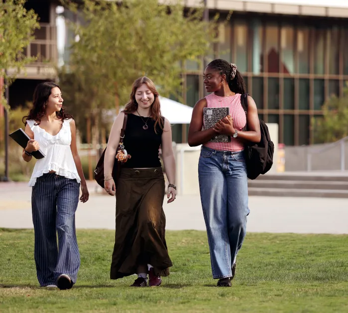 Three female students in conversation walking across the quad.