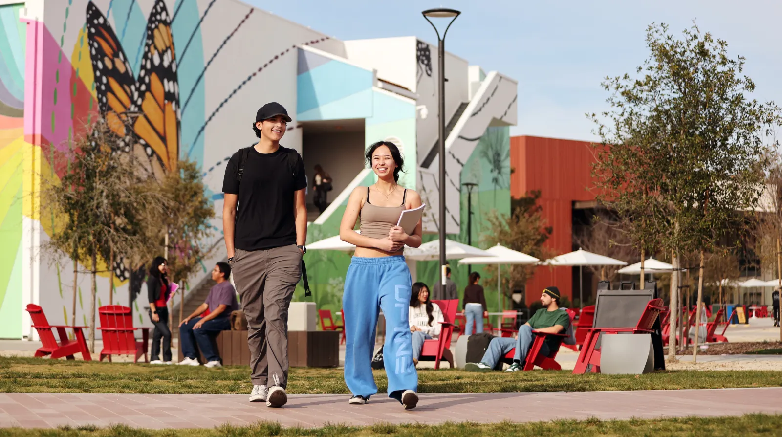 A male and female student walking in front of a building with a large colorful butterfly mural.
