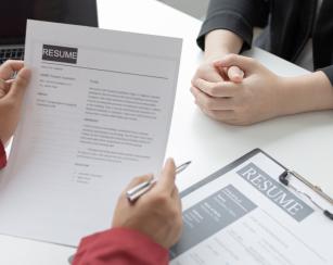 One person holding a resume and providing feedback to the other person who the resume belongs to.