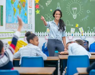 Teacher at the front of the classroom pointing to a student who has their hand raised.