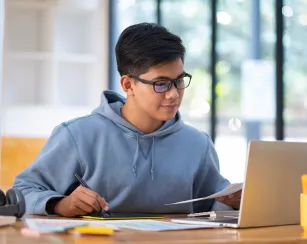 Young collage student using computer and mobile device studying online.