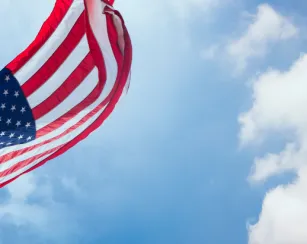 American flag waving with blue sky and cloud behind
