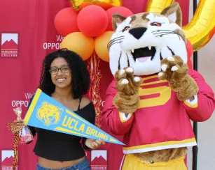 saddleback college mascot, blaze the bobcat, standing with a female student holding a UCLA pennant 