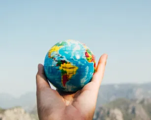 hands holding earth globe in front of mountains