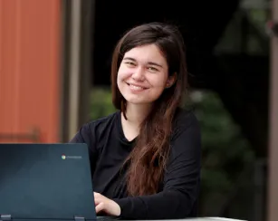 image of a female student sitting at a table outside of the gateway building with her laptop