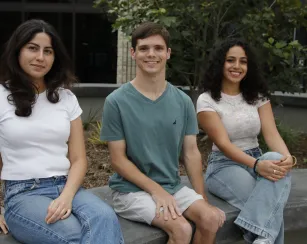 Three students sitting on the planter box smiling at camera