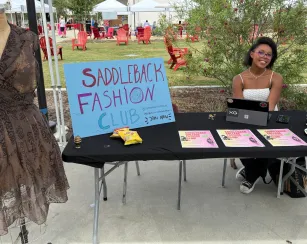 A student sits at a table for the Saddleback Fashion Club. Near her is a a body form with a brown lace dress.