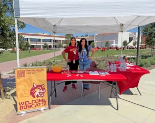Two female employees of Saddleback College stand at a welcome booth ready to provide information and answer questions.