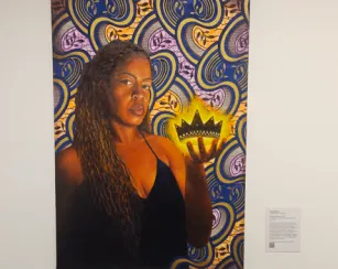 Painting of a woman with long locs and a black dress holding a glowing gold crown above her palm, set against a vibrant, swirling blue, purple, and gold patterned background.