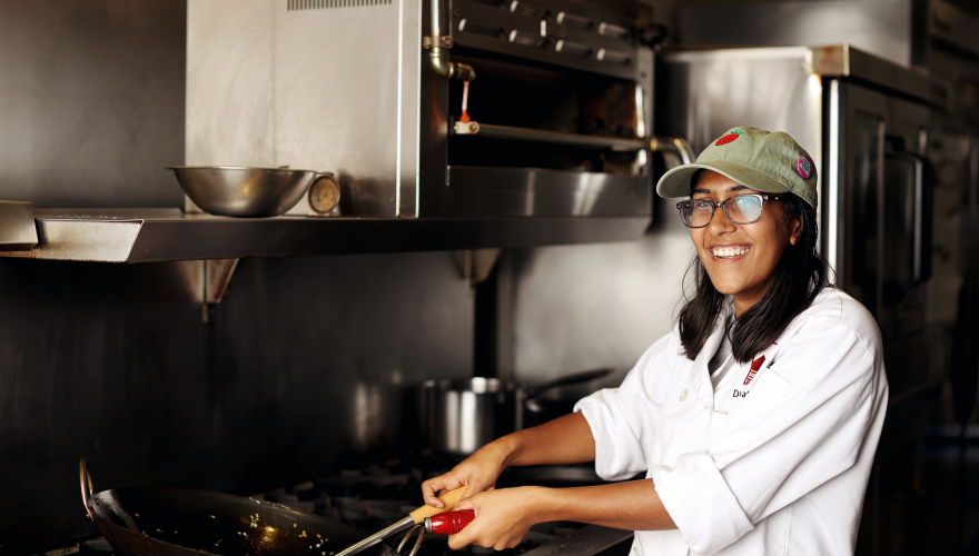 Culinary arts student holding pan at stove.