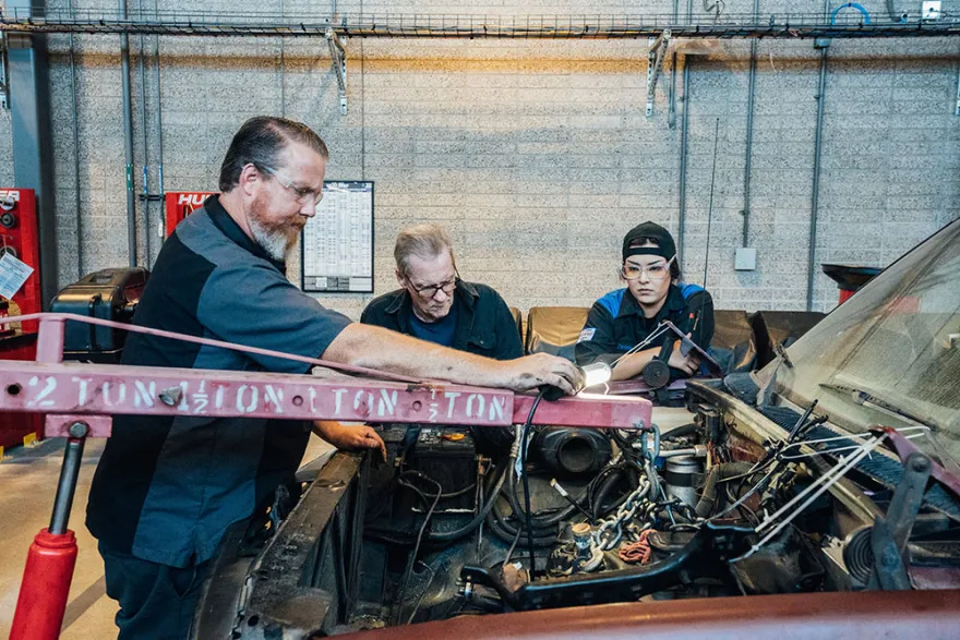Teacher and students at lowering an engine block into a car.